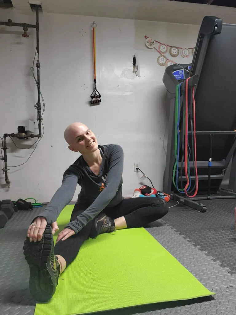 A woman sitting on a yoga mat in a gym stretching with one leg out.