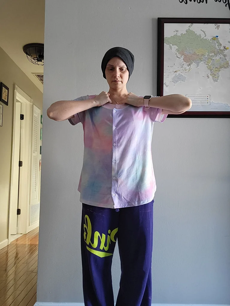 A woman standing with a grip on the inside of the collar of her shirt.