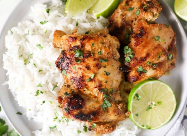 plate with white rice, cut limes, and two pieces of cilantro chicken
