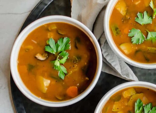 overhead shot of three bowls of soup on a tray with spoons and a napkin
