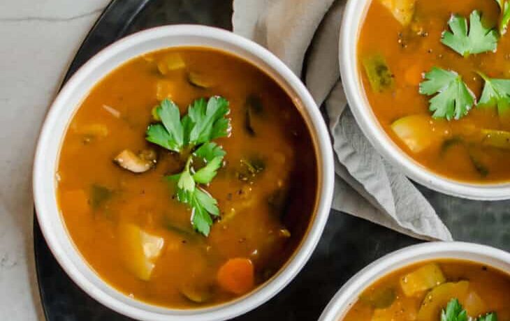 overhead shot of three bowls of soup on a tray with spoons and a napkin