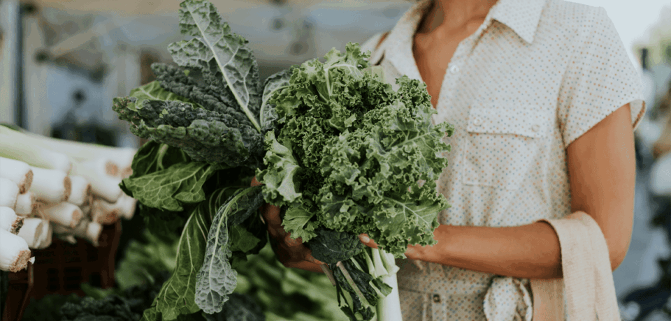 a women shopping holding a bundle of leafy greens in her hand