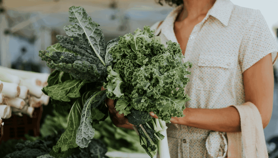 a women shopping holding a bundle of leafy greens in her hand